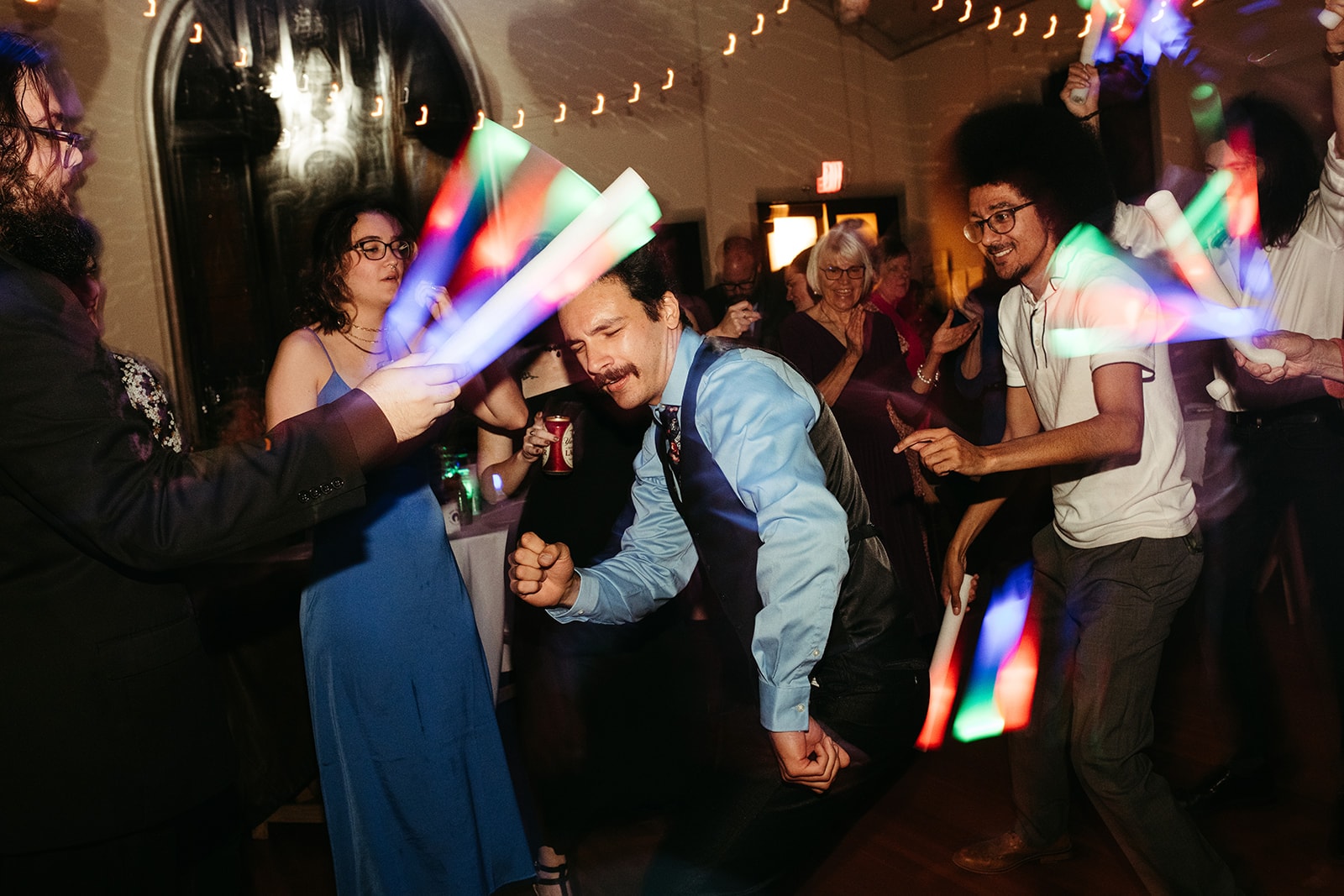Guests dancing with glow sticks beneath strings of café lights on the Sanctuary dancefloor